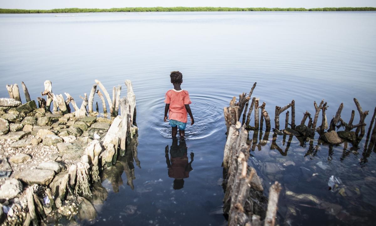 A young girl wades into water where the family kitchen once stood in Diamniadio Island, Saloum Delta in Senegal. Rising water levels caused by rising global temperatures have led to frequent flooding in the delta. The rising sea also has increased salt levels in the nearby water, poisoning the soil and killing crops. Photo © Jane Hahn/AP.
